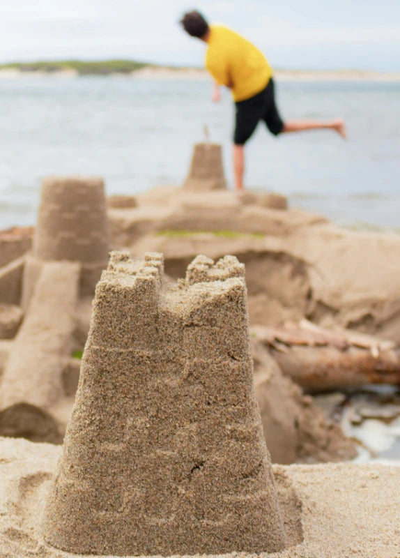 Photograph of a sand castle on the beach with kids in the background